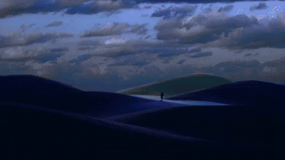 A person walking across dark, rolling dunes under a dramatic, cloudy sky in a looping animation.